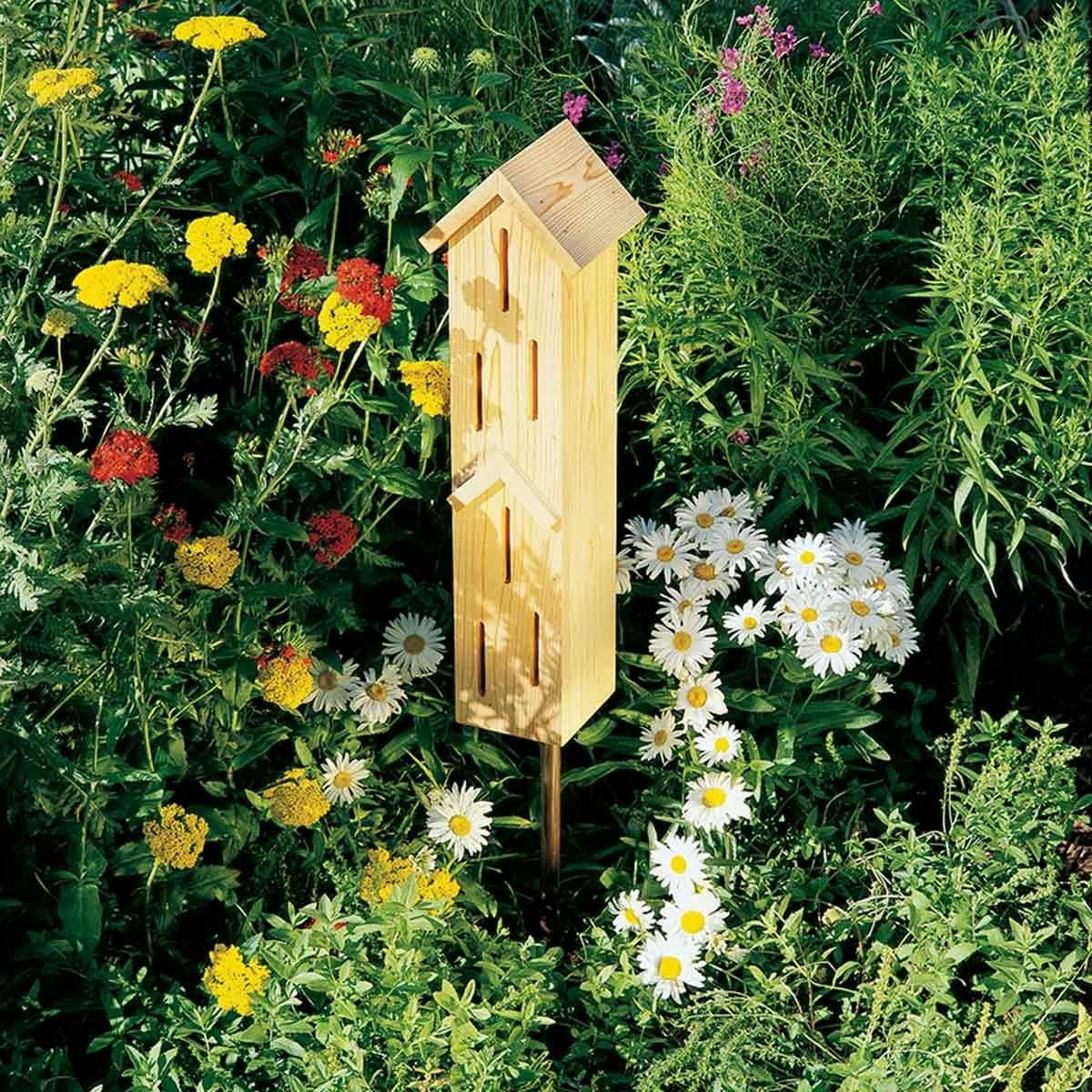 A wooden insect hotel surrounded by colorful wildflowers in a garden.