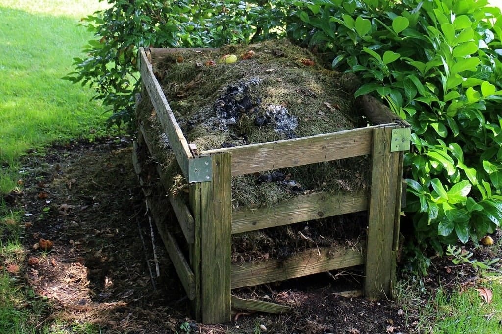 A wooden compost bin filled with organic materials, surrounded by greenery.